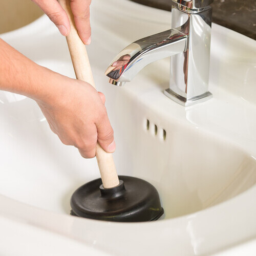 Plumber is cleaning sink with plunger.