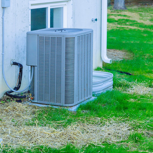 An air conditioner is being installed outside new house for residential use in immediate vicinity of building